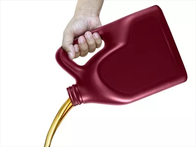 عکس ریختن روغن موتور از قوطی در دست بر روی پس زمینه سفید
