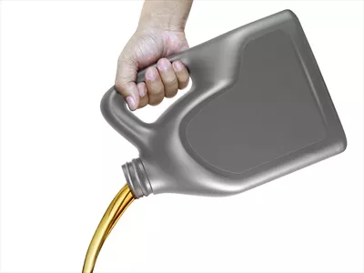عکس ریختن روغن موتور از قوطی در دست بر روی پس زمینه سفید