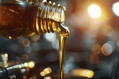 عکس ریختن روغن از ظرف به محفظه موتور با پس زمینه ای محو و قطعات خودرو در کانون توجه