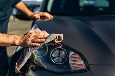 عکس مردی در حال تمیز کردن ماشین خود با دستمال میکروفیبر در خیابان