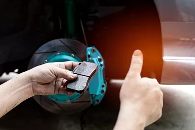 عکس بررسی ضخامت لنت ترمز توسط یک مرد و نشان دادن رضایت در خدمات خودرو