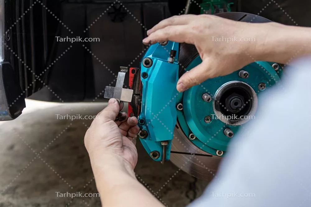 عکس مردی در حال تنظیم بخش هایی از کالیپر ترمز در کارگاه تعمیر خودرو