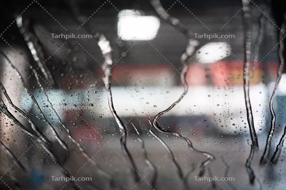 عکس نمایی از شستشوی خودرو با آب بر روی شیشه جلو از داخل ماشین