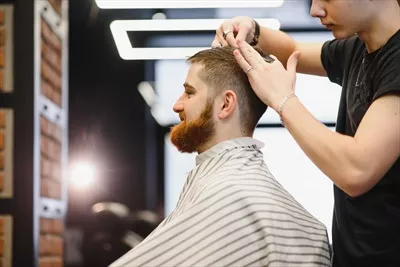 عکس آرایشگر جوان و خوش تیپ در حال اصلاح موی مردی با ریش جذاب
