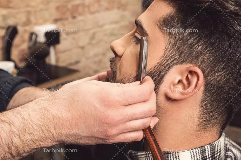 عکس آرایشگر در حال اصلاح ریش با تیغ مستقیم و دقت بالا
