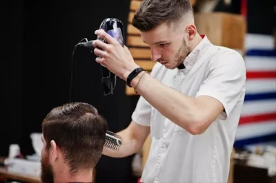 عکس مرد جوان با ریش در حال دریافت haircut توسط آرایشگر در آرایشگاه
