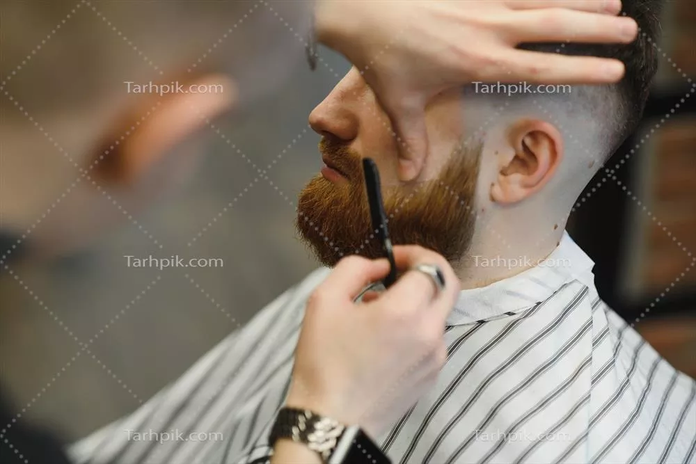 عکس تصویری نزدیک از آرایشگری که با تیغ فولادی مردی را اصلاح می کند