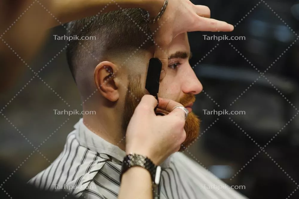 عکس تصویری نزدیک از آرایشگری که با تیغ فولادی مردی را اصلاح می کند