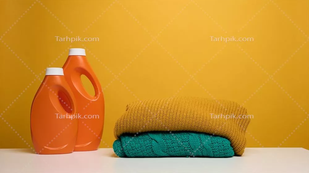 عکس تصویری از لباس های شسته و تا شده در کنار مایع شوینده نارنجی