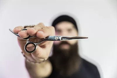 عکس آرایشگر با ریش بلند در حال استفاده از قیچی برای اصلاح موها