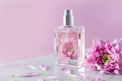 عکس بطری شفاف اسپری آرایشی یا عطر در کنار گل های زیبا و معطر بنفش