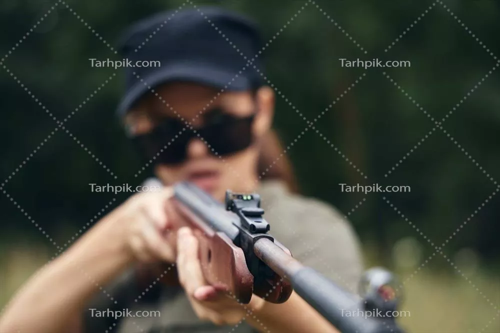 عکس زنی در دل طبیعت با عینک آفتابی و تفنگ در دست، در لباس سبز