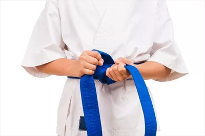 عکس پسر کوچک با کمربند آبی در حال بستن گره کمربند سیاه خود