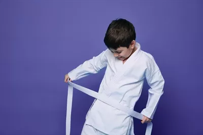 عکس پسر بچه ای شاد و با اعتماد به نفس در حال بستن کمربند کیک بوکسینگ خود