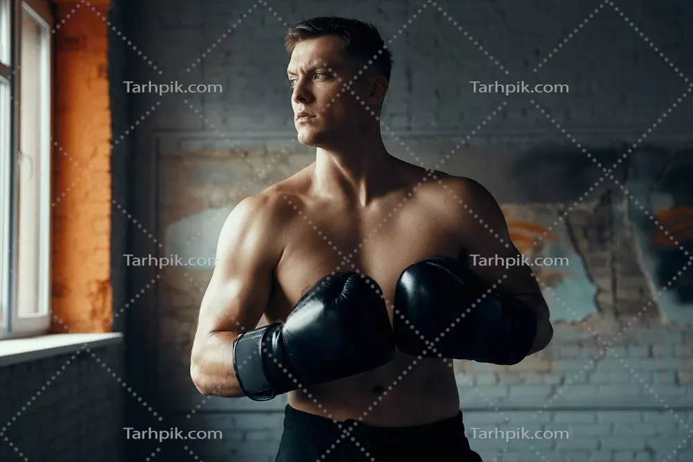 عکس مرد جوان با اعتماد به نفس در دستکش بوکس در حال نگاه کردن به دور
