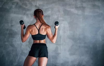 عکس زنی جوان و ورزشکار در باشگاه با دمبل در دستانش در حال تمرین