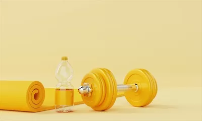 عکس مجموعه ورزشی شامل زیرانداز یوگا، بطری آب و دمبل بر روی پس زمینه زرد ملایم