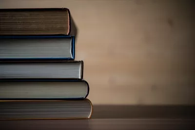 عکس مجموعه ای از کتاب ها بر روی یک میز چوبی زیبا و دلنشین