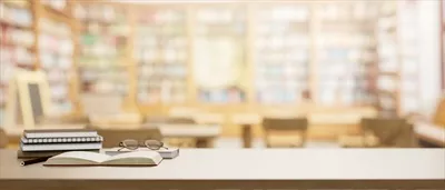 عکس میز چوبی با عینک، کتاب و فضای ارائه در کتابخانه مدرسه