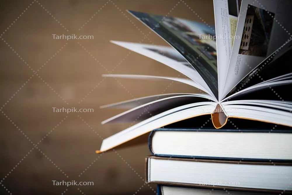 عکس تصویری زیبا از یک کتاب باز در کنار کتاب های جلد سخت بر روی میز چوبی