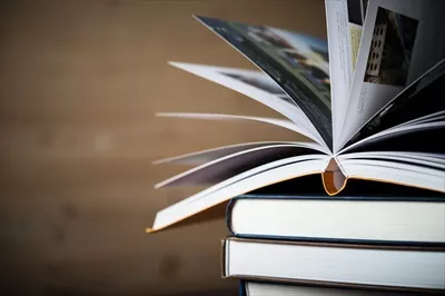 عکس تصویری زیبا از یک کتاب باز در کنار کتاب های جلد سخت بر روی میز چوبی