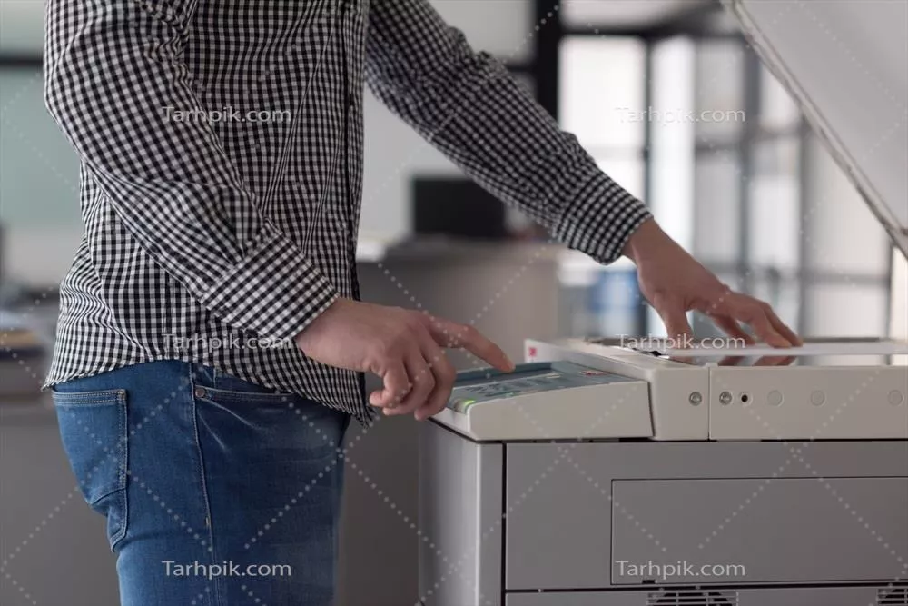 عکس مدیر جوان در حال کپی کردن اسناد اداری با دقت و تمرکز