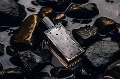 عکس بطری عطر شیک و مدرن با طراحی شیشه ای در میان سنگ های سیاه در باران