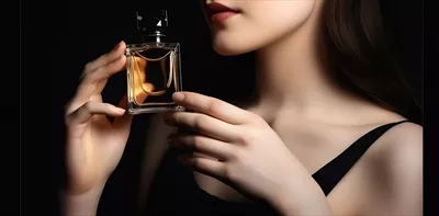 عکس زنی جوان و زیبا با بطری عطر در پس زمینه تاریک - نمای نزدیک