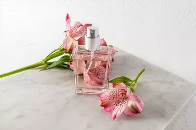 عکس عطر زنانه زیبا در کنار گل های صورتی و سنگ مرمر سفید
