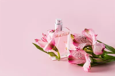 عکس عطر زنانه شیک در پس زمینه صورتی با گل های آسترومریا