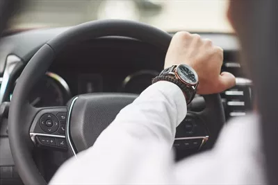 عکس یک تاجر در حال رانندگی با خودروی خود و نگاه به ساعتش