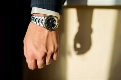عکس مردی با پیراهن سفید و کت تیره در حال نمایش ساعت لوکس و محدود