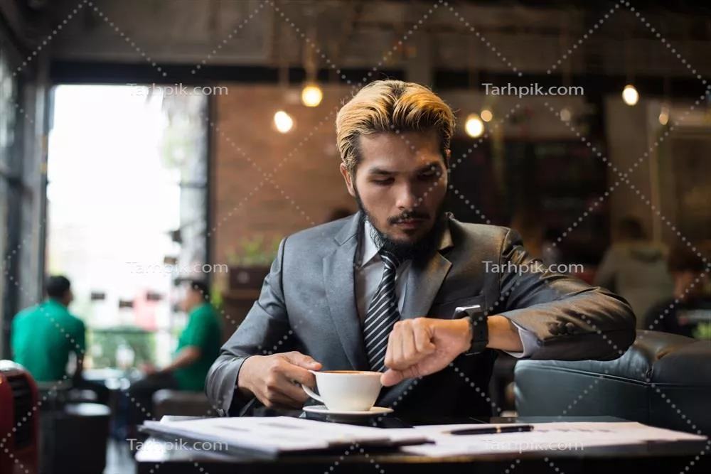عکس مردی که در کافه به ساعتش نگاه می کند و مشغول کار است