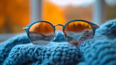 عکس عینک آفتابی با طرح لاک پشتی قهوه ای بر روی یک ژاکت بافتنی در غروب زمستانی