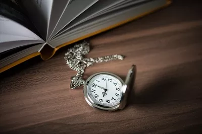 عکس نگاهی نزدیک به یک ساعت جیبی طلایی و کتابی قدیمی