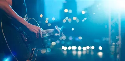 عکس گیتاریست در حال اجرا بر روی صحنه با پس زمینه نرم و محو
