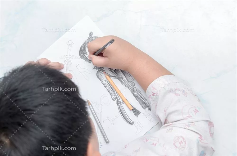 عکس تصویری از یک پسر دانش آموز در حال کشیدن نقاشی با مداد رنگی