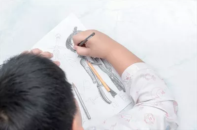 عکس تصویری از یک پسر دانش آموز در حال کشیدن نقاشی با مداد رنگی