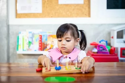 عکس دختر بچه ای که با اسباب بازی های چوبی در حال بازی است