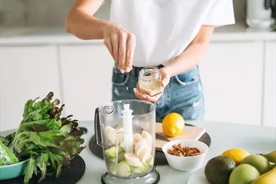 عکس زنی جوان و لاغر در حال تهیه اسموتی میوه ای سالم در آشپزخانه