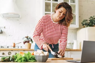 عکس زنی جوان و با اعتماد به نفس در سایز بزرگ در حال آشپزی با لپ تاپ در خانه