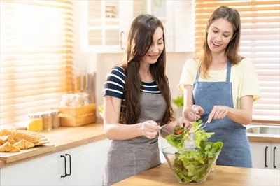 عکس زوج همجنس گرا با لبخند در حال تهیه سالاد در آشپزخانه