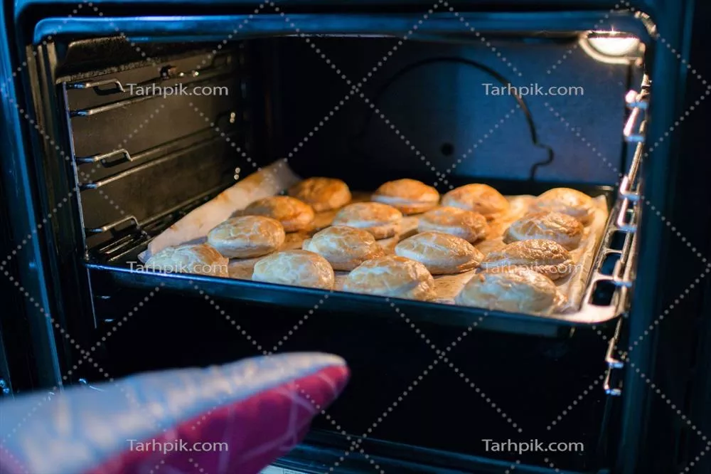 عکس دست انسان با دستکش فر، سینی پر از پیراشکی را از فر خارج می کند