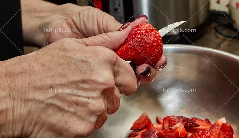 عکس آشپز در حال برش توت فرنگی برای دسر در آشپزخانه خانگی