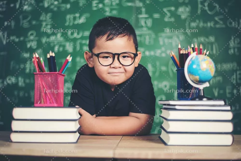 عکس پسرک اندیشمند با کتاب در کنار تخته سیاه مدرسه