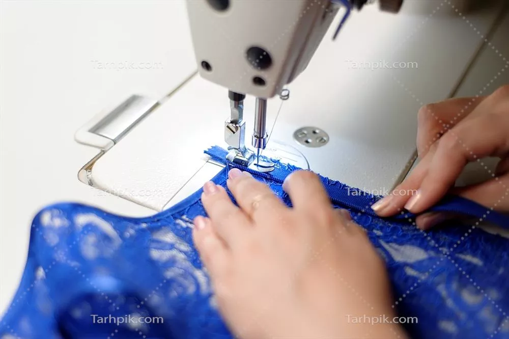 عکس زن خیاط در حال دوختن پارچه آبی با دقت و مهارت بالا