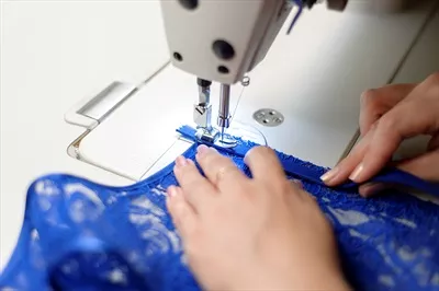 عکس زن خیاط در حال دوختن پارچه آبی با دقت و مهارت بالا