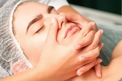 عکس زنی جوان و سفیدپوست در حال دریافت ماساژ صورت در یک اسپا
