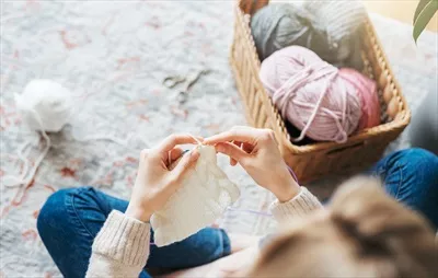 عکس زنی جوان در حال بافتن شال گرم در فضای داخلی منزل