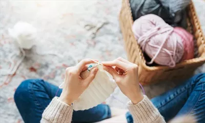 عکس زنی جوان در حال بافتن شال گرم در فضای داخلی منزل